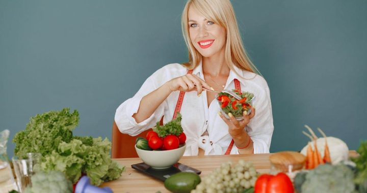 Blonde woman enjoying a fresh salad surrounded by vegetables, promoting healthy eating.