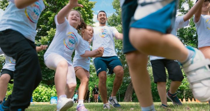 Joyful group of children and adult engaging in playful activities in a sunny park setting.