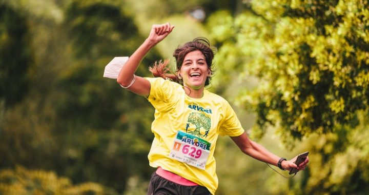 Joyful female runner in yellow participates in an outdoor race amidst lush greenery, embodying athletic enthusiasm.