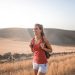 Smiling woman in casual attire enjoying a summer hike through golden fields at sunset.